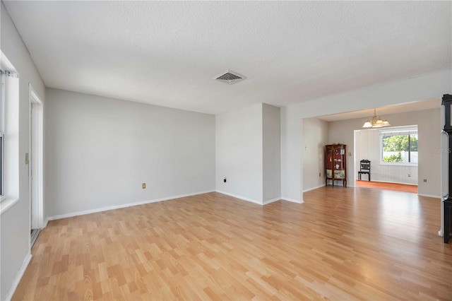 spare room with a chandelier, light wood-style floors, visible vents, and baseboards