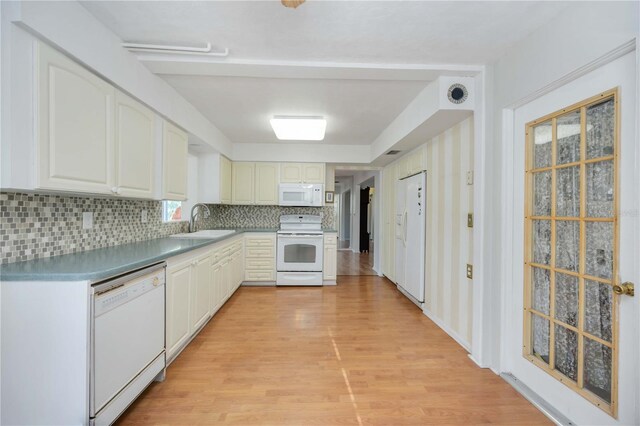 kitchen with white appliances, a sink, light wood-type flooring, decorative backsplash, and white cabinetry