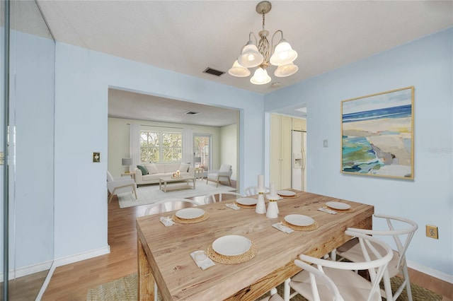 dining space featuring a chandelier, light wood finished floors, and baseboards