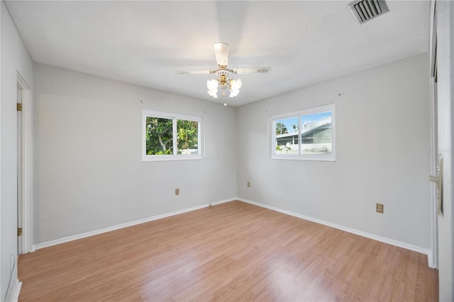 spare room featuring light wood finished floors, a ceiling fan, plenty of natural light, and visible vents
