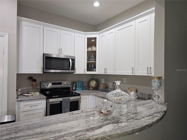 kitchen with appliances with stainless steel finishes, white cabinetry, glass insert cabinets, light stone countertops, and recessed lighting