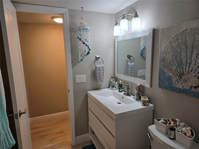 half bath featuring wood finished floors, vanity, toilet, and baseboards