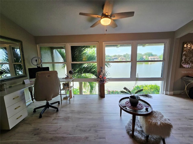 home office with plenty of natural light, a ceiling fan, wood finished floors, and a water view