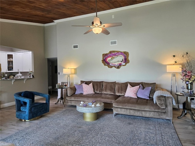 living area featuring wood ceiling, wood finished floors, ceiling fan, a towering ceiling, and ornamental molding