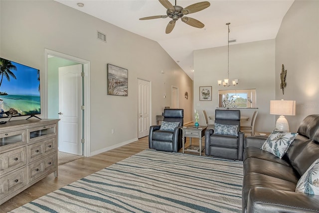 living room with a chandelier, ceiling fan, light wood finished floors, baseboards, and high vaulted ceiling