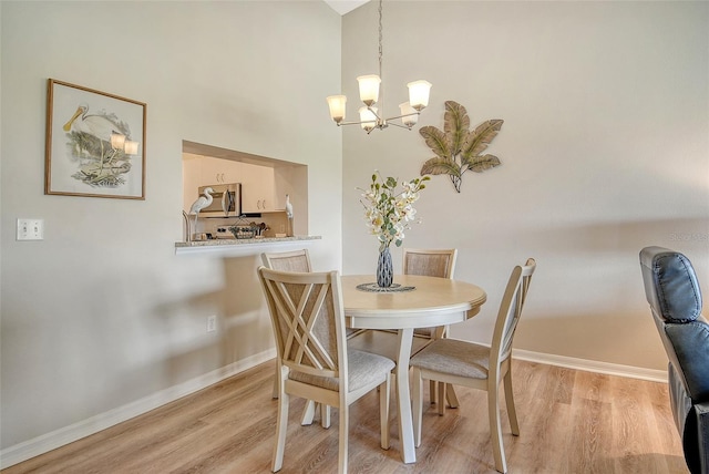 dining area with a chandelier, baseboards, light wood-type flooring, and a towering ceiling