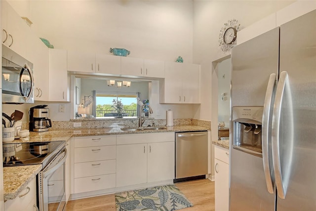 kitchen featuring stainless steel appliances, a sink, a towering ceiling, light wood-type flooring, and white cabinets