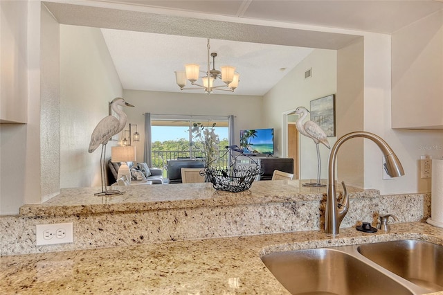 kitchen featuring a sink, a chandelier, open floor plan, light stone countertops, and decorative light fixtures