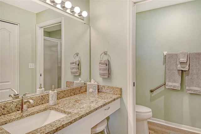 bathroom with vanity, wood finished floors, toilet, a stall shower, and baseboards