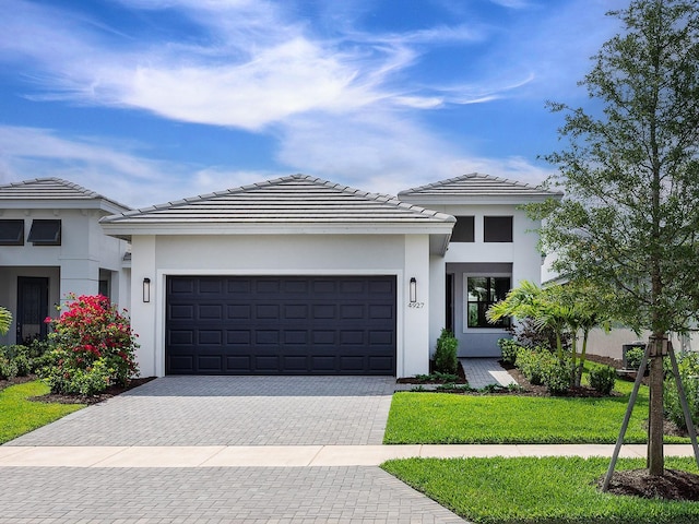 prairie-style home with an attached garage, decorative driveway, stucco siding, and a front yard