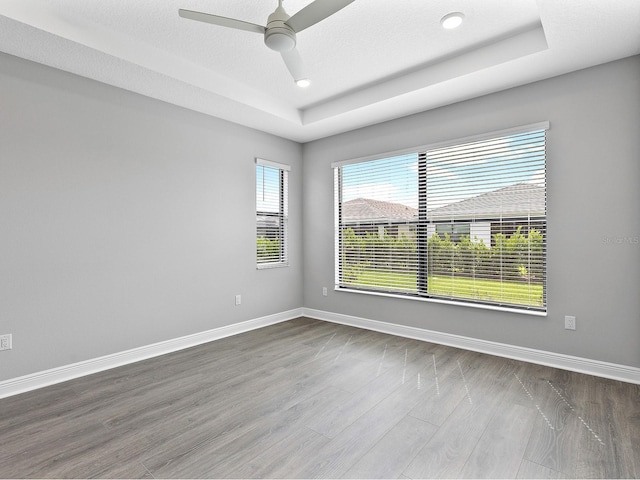 unfurnished room with a raised ceiling, dark wood finished floors, a ceiling fan, baseboards, and recessed lighting