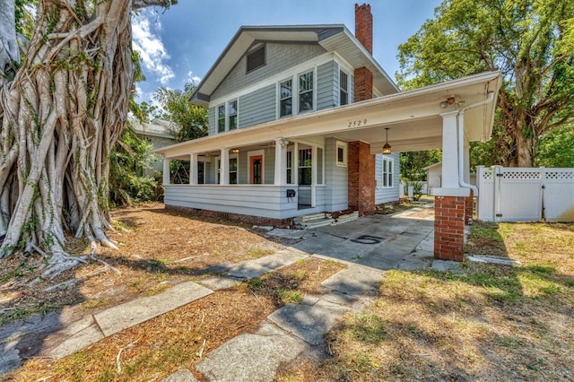 view of front of house with a chimney, covered porch, fence, a carport, and a gate