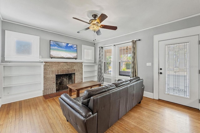 living room with light wood finished floors, a brick fireplace, a ceiling fan, and ornamental molding