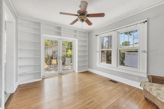 spare room featuring light wood finished floors, built in features, ceiling fan, and baseboards