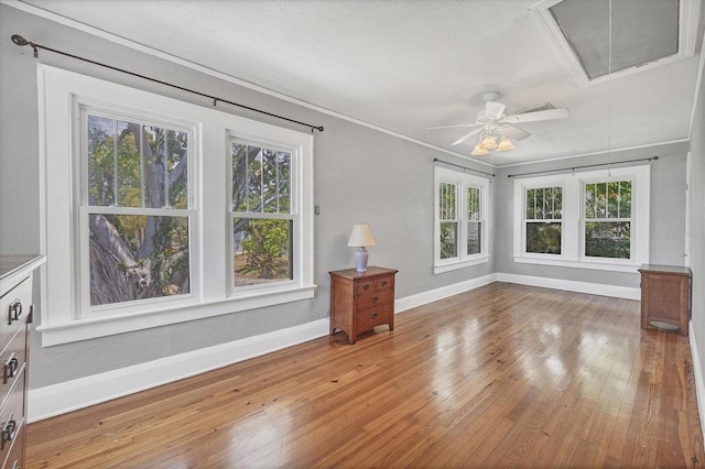 spare room featuring attic access, plenty of natural light, baseboards, wood-type flooring, and ornamental molding