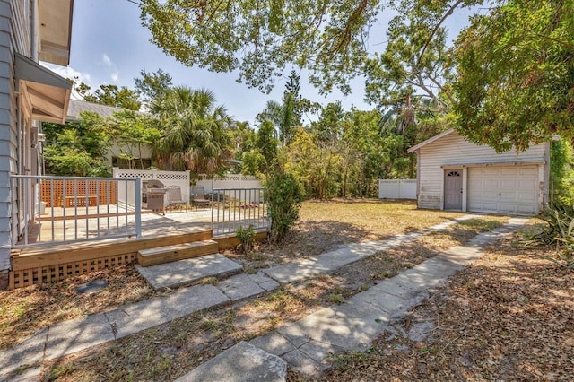 view of yard featuring a wooden deck, fence, a detached garage, and an outbuilding