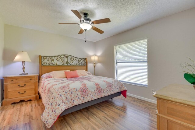 bedroom with light wood-type flooring, baseboards, ceiling fan, and a textured ceiling
