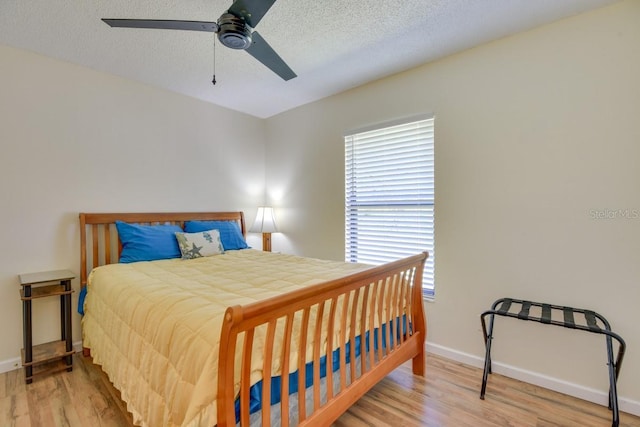 bedroom featuring wood finished floors, multiple windows, baseboards, and a textured ceiling