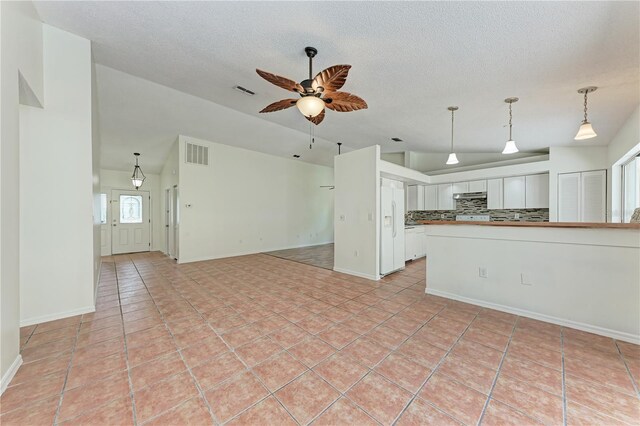 unfurnished living room with vaulted ceiling, a textured ceiling, ceiling fan, light tile patterned floors, and baseboards