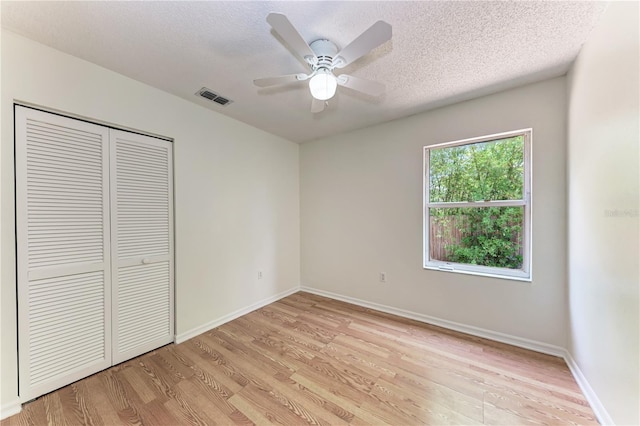 unfurnished bedroom with light wood-style flooring, a closet, baseboards, a textured ceiling, and ceiling fan