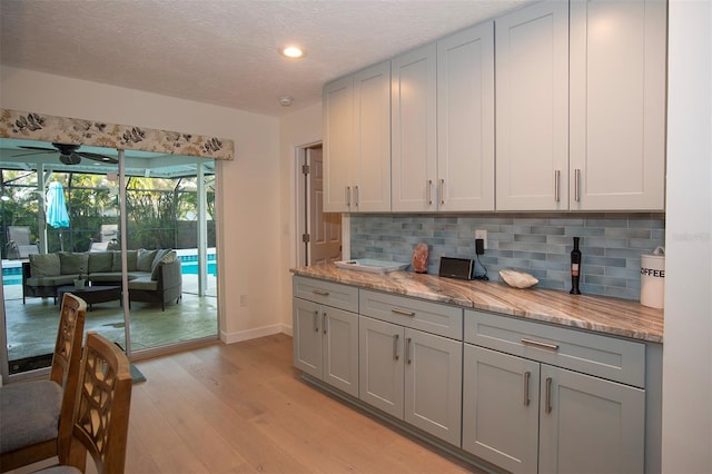 kitchen featuring gray cabinetry, light wood-style flooring, decorative backsplash, baseboards, and recessed lighting