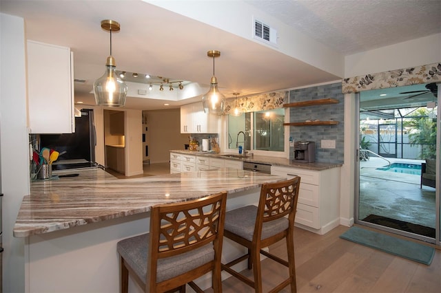kitchen with a sink, light wood finished floors, white cabinetry, light stone counters, and a peninsula