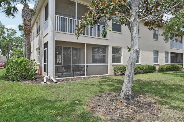 rear view of property with stucco siding, a yard, and a sunroom