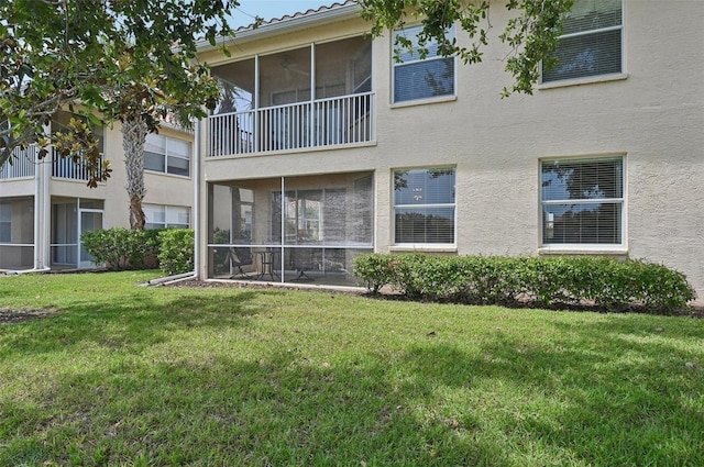 rear view of property with stucco siding, a sunroom, and a lawn