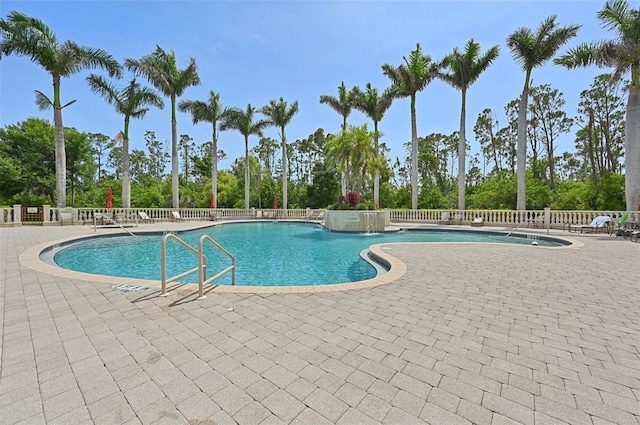 community pool featuring a patio area, view of wooded area, and fence
