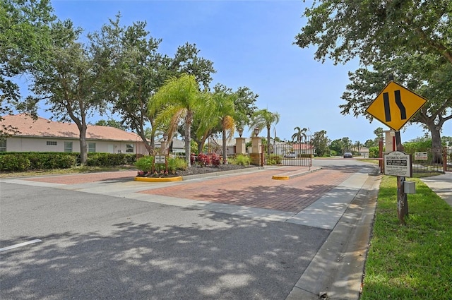 view of decorative street with curbs, a gate, traffic signs, sidewalks, and a gated entry