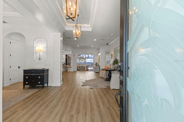 foyer with ornamental molding, a chandelier, light wood-style flooring, arched walkways, and a tray ceiling