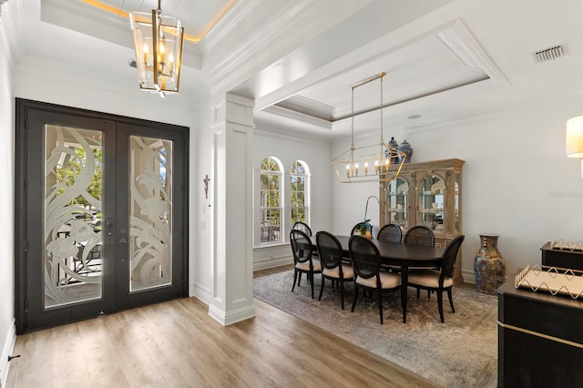 dining room featuring a raised ceiling, a chandelier, wood finished floors, french doors, and ornamental molding