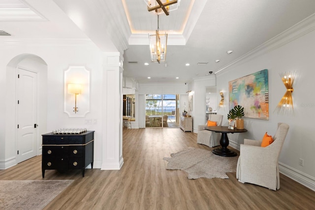 foyer entrance with wood finished floors, ornamental molding, baseboards, arched walkways, and a chandelier