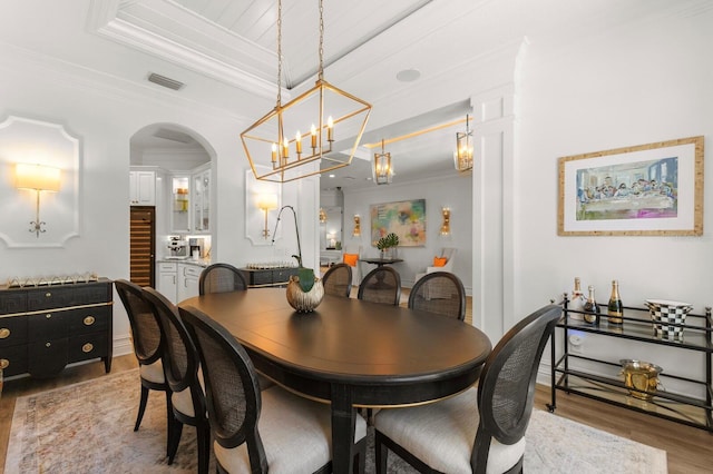 dining space featuring ornamental molding, light wood-type flooring, a chandelier, and arched walkways
