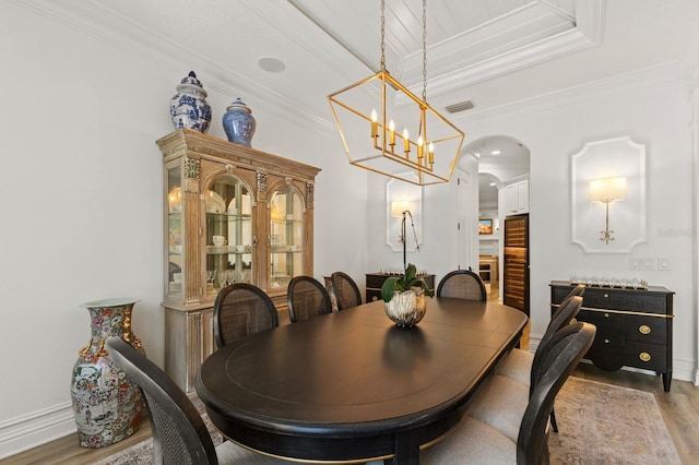 dining space with arched walkways, wood finished floors, ornamental molding, baseboards, and a chandelier