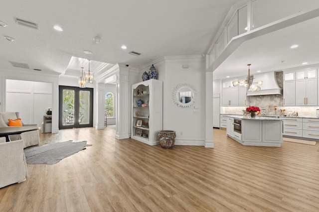 kitchen featuring custom exhaust hood, open floor plan, a chandelier, crown molding, and decorative backsplash
