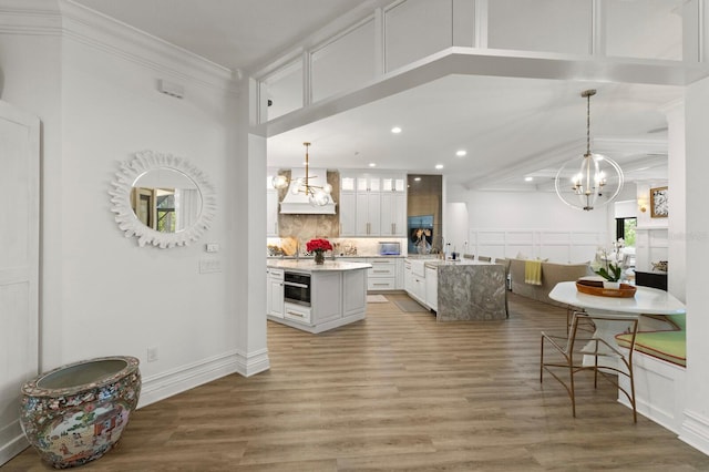 kitchen featuring a chandelier, an island with sink, recessed lighting, custom range hood, and crown molding
