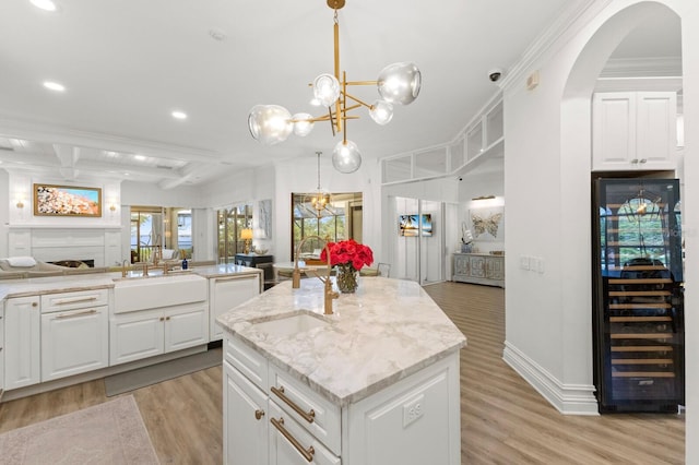 kitchen with beverage cooler, a sink, open floor plan, light wood-style floors, and a kitchen island with sink