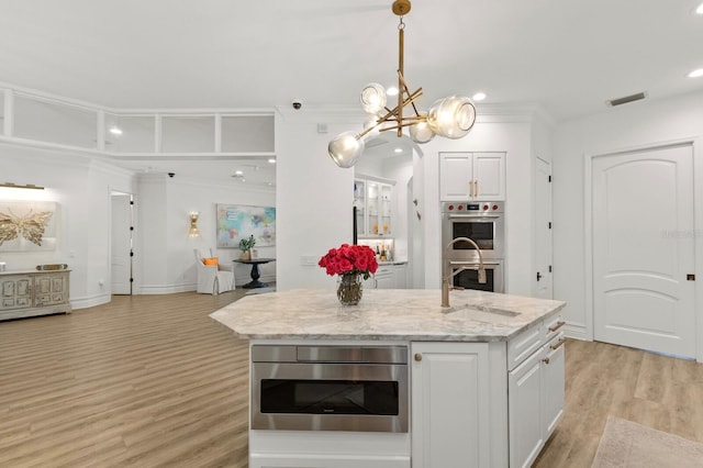 kitchen featuring a sink, stainless steel double oven, white cabinetry, light wood-type flooring, and a chandelier