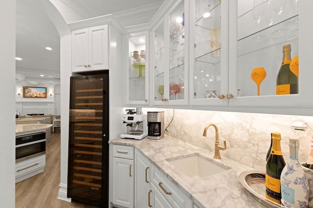 indoor wet bar featuring beverage cooler, light wood finished floors, crown molding, recessed lighting, and tasteful backsplash