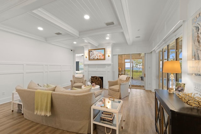 living area with a decorative wall, beamed ceiling, wood finished floors, crown molding, and a fireplace