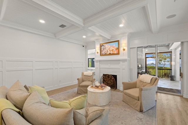 living area with light wood-type flooring, a decorative wall, beamed ceiling, healthy amount of natural light, and a fireplace