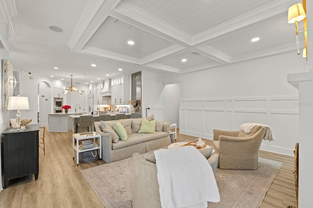 living room featuring beam ceiling, light wood-style flooring, crown molding, arched walkways, and a decorative wall