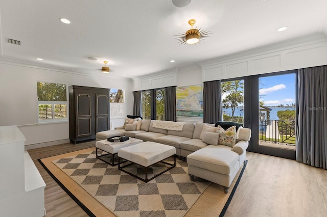 living room with light wood-type flooring, crown molding, plenty of natural light, recessed lighting, and a water view