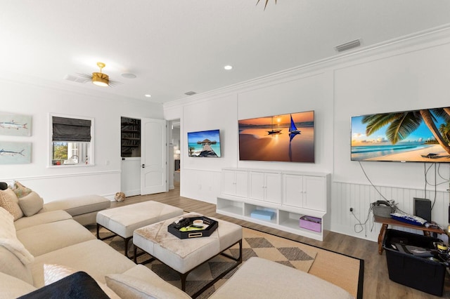 living area featuring wood finished floors, crown molding, recessed lighting, and a wainscoted wall