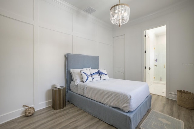 bedroom with wood finished floors, a chandelier, baseboards, crown molding, and ensuite bath
