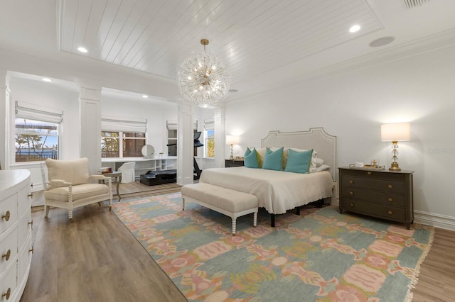 bedroom featuring decorative columns, wood finished floors, crown molding, a chandelier, and baseboards