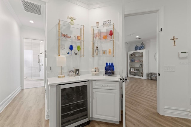 indoor dry bar featuring wine cooler, light wood-style floors, ornamental molding, and baseboards