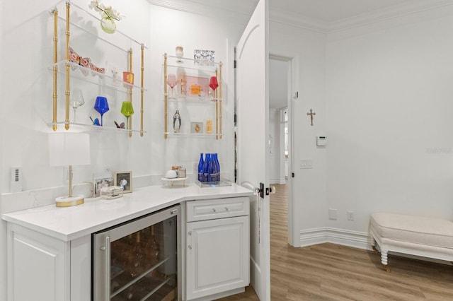 indoor dry bar featuring beverage cooler, ornamental molding, light wood finished floors, and baseboards