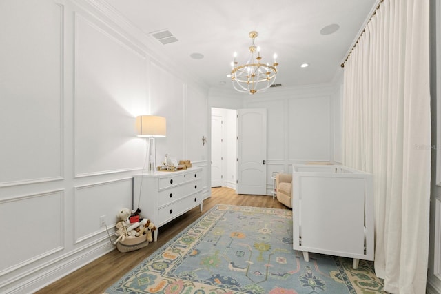 bedroom with a decorative wall, a chandelier, wood finished floors, crown molding, and recessed lighting